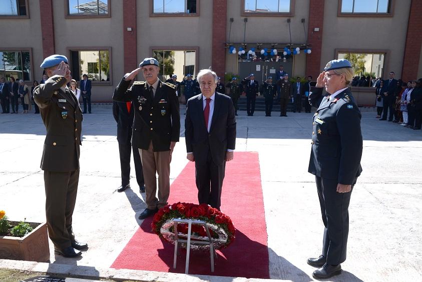 UN officials and military personnel stand on a red carpet during a wreath-laying ceremony outside a building.