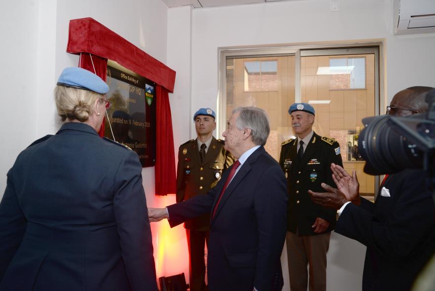 UN Secretary General Guterres unveils a plaque indoors during a formal ceremony, with uniformed personnel and others standing nearby.